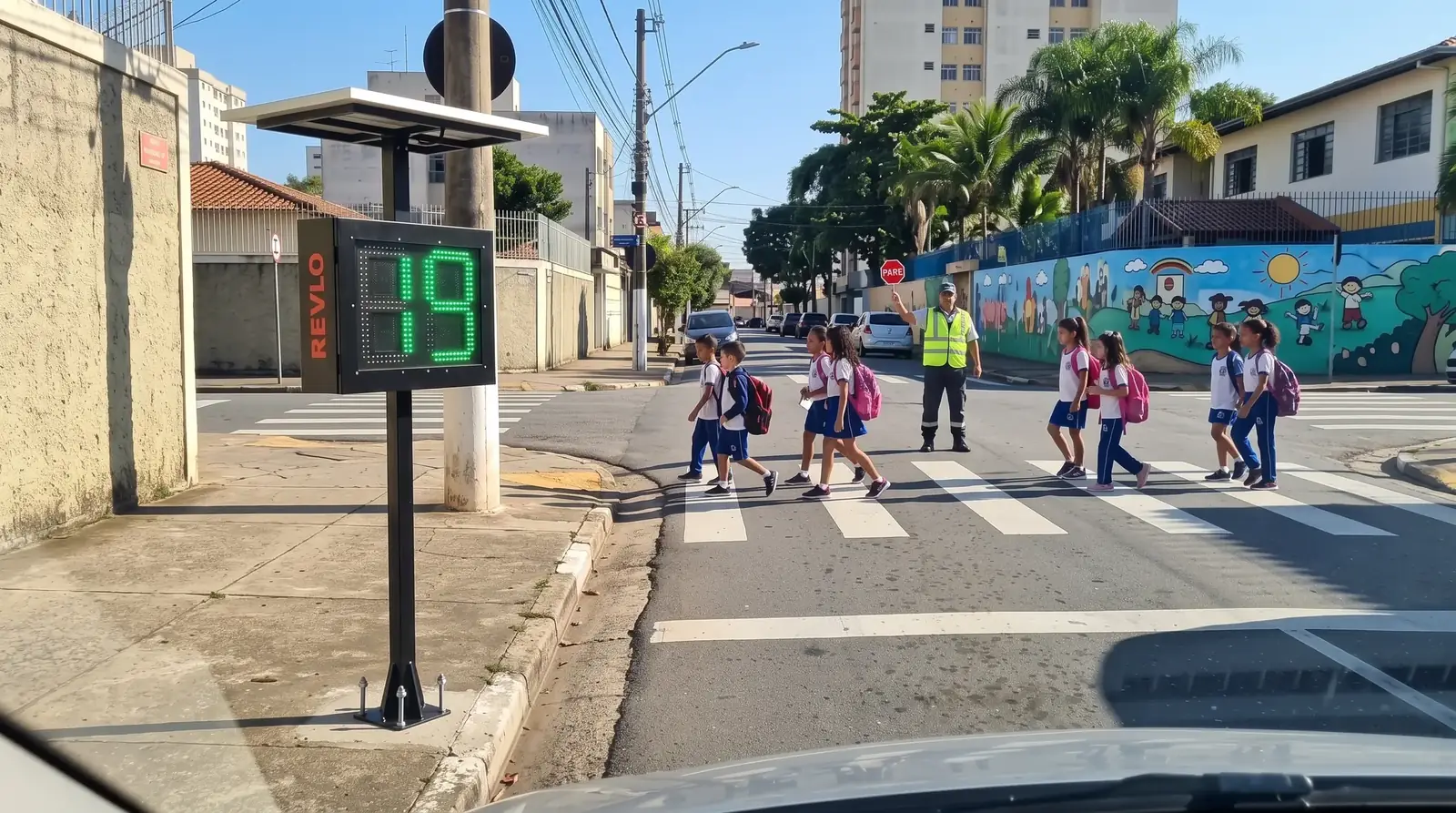 Lombada educativa Revlo na calçada de uma escola, mostrando 19 enquanto crianças atravessam a faixa